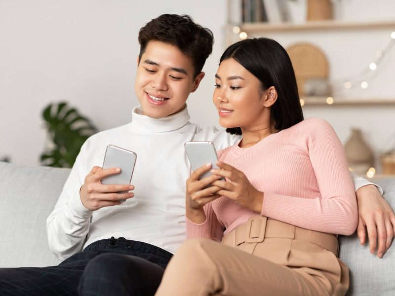 asian-couple-using-smartphone-phones-browsing-internet-sitting-at-home-1.jpg